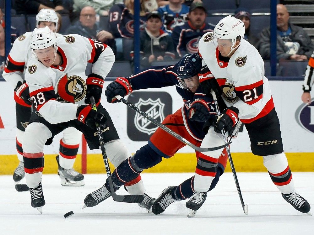 Liam Foudy of the Columbus Blue Jackets loses his edge while chasing after the puck against Patrick Brown #38 and Mathieu Joseph #21 of the Ottawa Senators during the third period.
