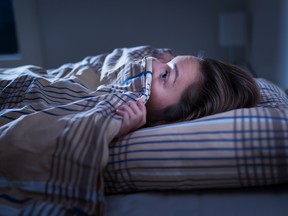 Scared woman hiding under blanket unable to sleep after nightmare.