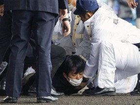 A man, believed to be a suspect who threw a pipe-like object near Japanese Prime Minister Fumio Kishida during his outdoor speech, is held by police officers at Saikazaki fishing port in Wakayama, Japan, Saturday, April 15, 2023.