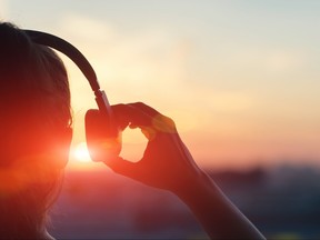 Woman lifting one side of headphones from ear at sunset.