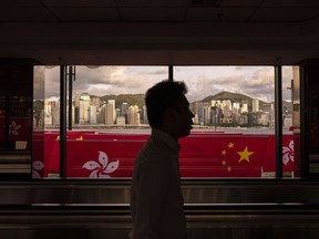 A pedestrian walks through a footbridge as Chinese and Hong Kong flags are strung to mark the 26th anniversary of the city's handover from Britain to China in Hong Kong, Tuesday, June 27, 2023. Ottawa is condemning Hong Kong officials for issuing bounties for the arrest of eight activists living abroad, days after Canada's peers slammed the move.