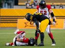 Tiger-Cats defensive end Mason Bennett (90) and Redblacks offensive lineman Zack Pelehos (52) check on  quarterback Jeremiah Masoli after he was hurt on a play in the first half of Saturday's game in Hamilton..