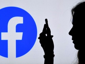 A person looks at a smart phone with a Facebook App logo displayed on the background.