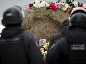 Police officers watch as people lay flowers paying the last respect to Alexei Navalny at the monument, a large boulder from the Solovetsky islands, where the first camp of the Gulag political prison system was established, in St. Petersburg, Russia on Saturday, Feb. 17, 2024. Russian authorities say that Alexei Navalny, the fiercest foe of Russian President Vladimir Putin who crusaded against official corruption and staged massive anti-Kremlin protests, died in prison. He was 47.