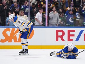 Buffalo Sabres' Rasmus Dahlin (26) lies on the ice as Tage Thompson (72) looks on while fans Vancouver Canucks celebrate.