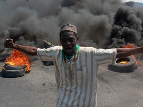 A man protests in Haiti, with tires burning in the background.
