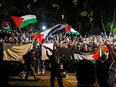 Pro-Palestinian demonstrators wave flags and hold up smartphones outside the fenced in area of an encampment on the University of Toronto campus on May 2, 2024.