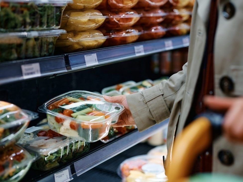 Primer plano de una mujer tomando verduras en un paquete de plástico mientras compra alimentos en el supermercado.