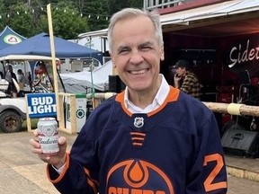 Bank of Canada Governor grinning while posing in Oilers jersey and holding can of Budweiser.