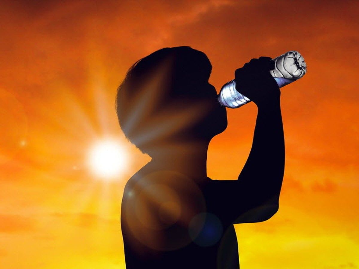 The silhouette of a man drinking from a water bottle.