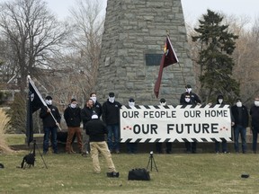 Members of an alt-right group, some with All Thy Sons monogrammed jackets and sporting a version of a modified former Canadian Red Ensign, record a video at the cenotaph at Sullivan's Pond in Dartmouth Sunday.