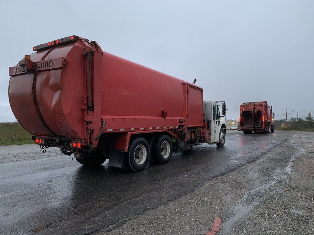 A garbage truck waits in line behind another one