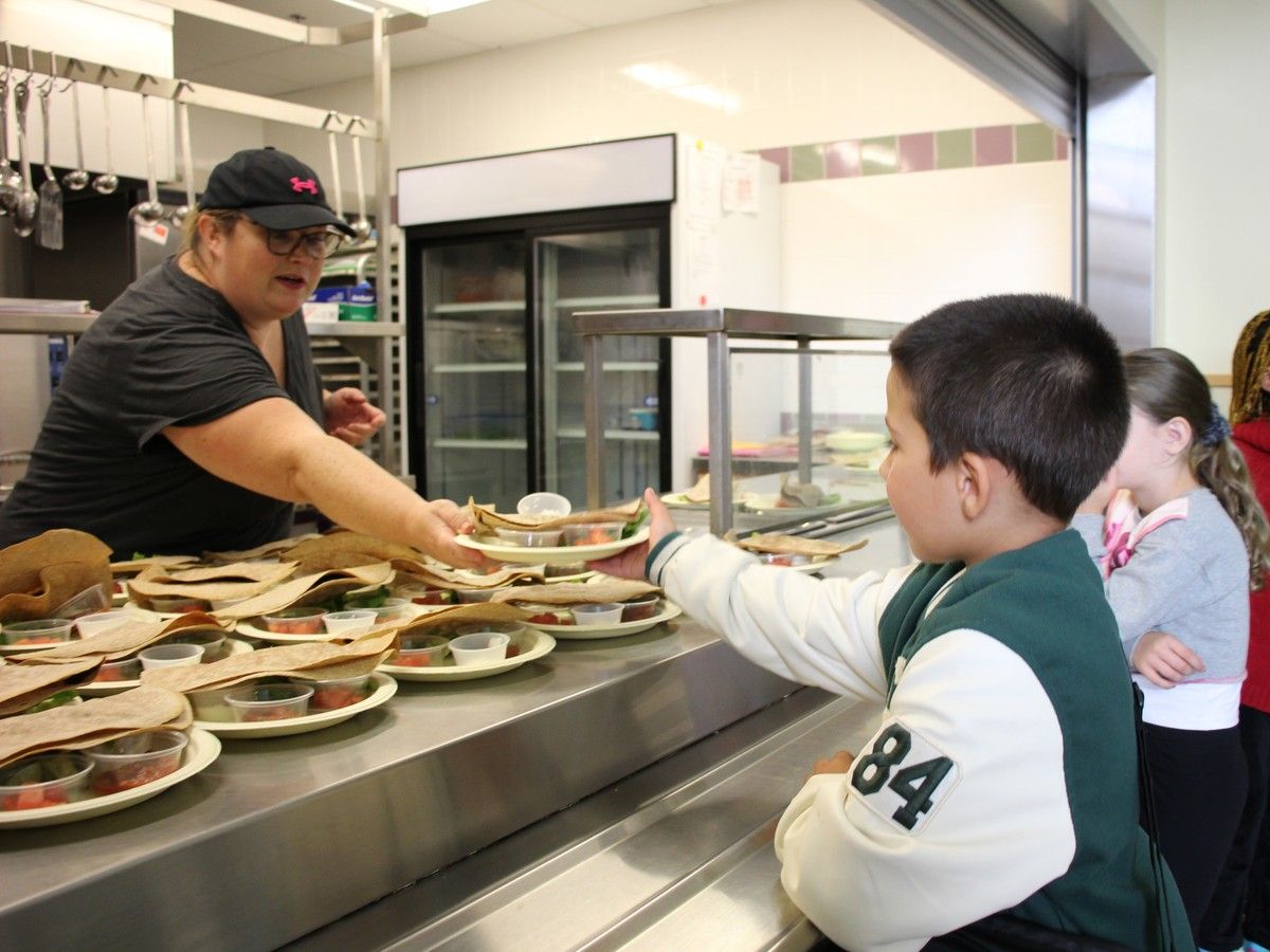 St. Anne's Elementary School Grade 3 student Kai Fraser takes his lunch from Genevieve Howie, who owns the catering company that is contracted to provide the provincially funded lunches at the Glace Bay school, on Oct. 1, 2024 - the first day of phase 1 of the program.
