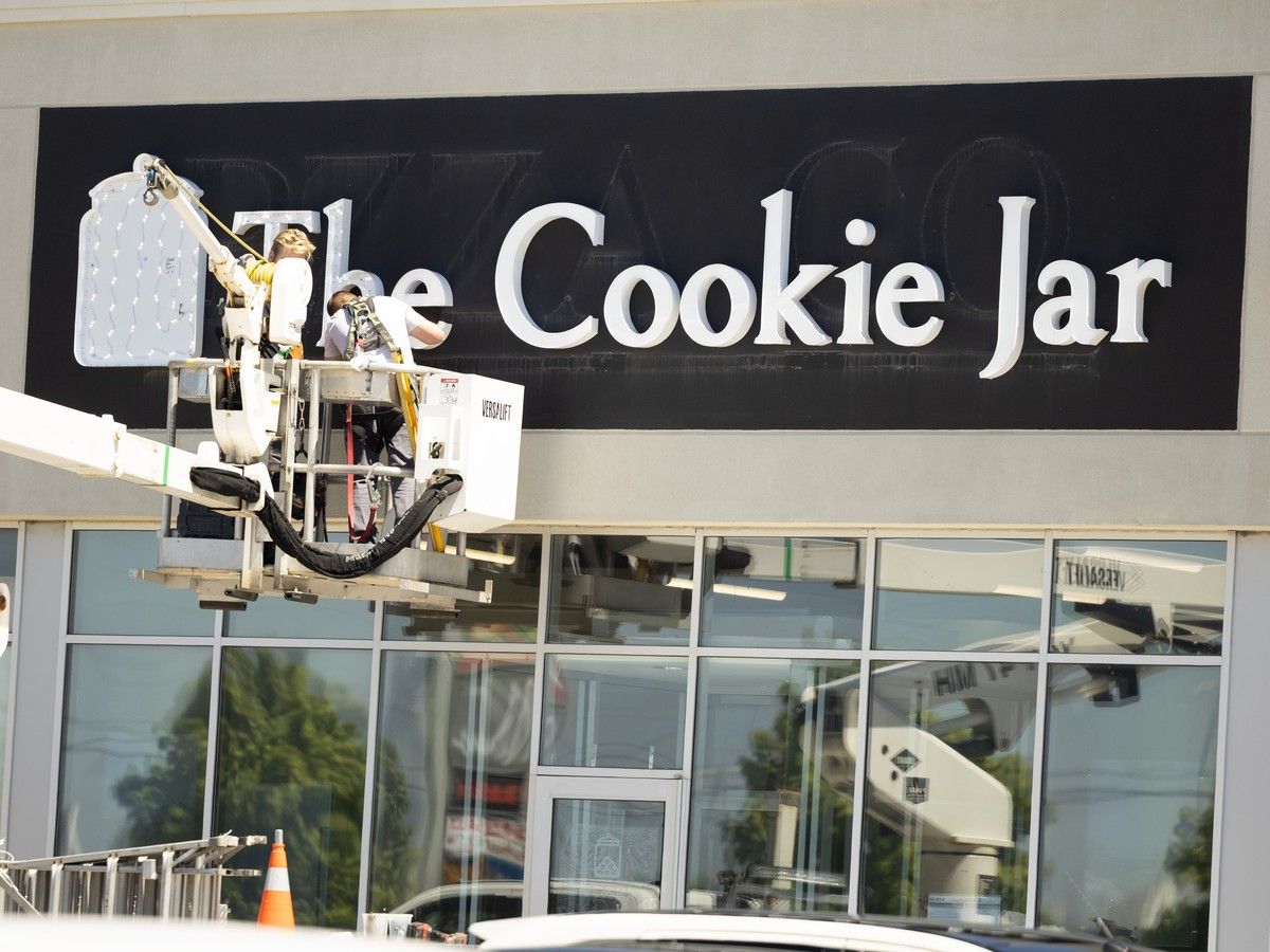 workers install a sign for a new gourmet cookie shop called the cookie jar in the bedford commons on wednesday.