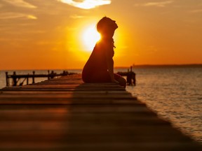 silhouette of a pregnant woman in a red dress sitting on pier at sunset