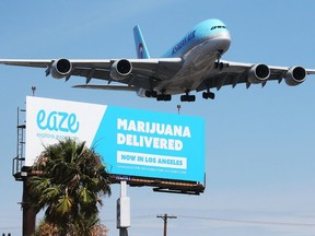 FILE: An airplane descends to land at Los Angeles International Airport above a billboard advertising the marijuana delivery service Eaze on July 12, 2018 in Los Angeles, Calif. /