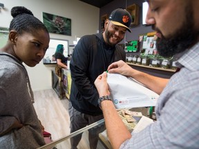 Budtender Danny Buelna (R) shows customers Mariah Roy (L) and Edward Ochoa (C) how to use the required child-proof bag for their purchases at the Green Pearl Organics dispensary on the first day of legal recreational marijuana sales in California, January 1, 2018 in California.