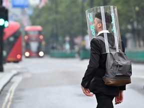 A pedestrian wearing a form of PPE (personal protective equipment) of a perspex full-face covering, as a precautionary measure against COVID-19, walks across Oxford Street in central London on June 11, 2020.