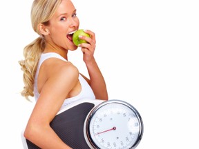 Young woman eating apple and carrying a weight scale over white background