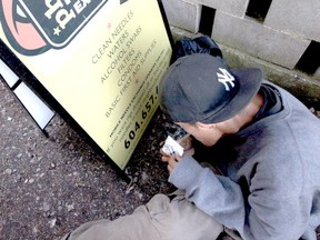An addict uses the sign for the Portland Hotel Society's mobile needle-exchange program to block the wind as he tries to smoke a rock of crack in a alley in Abbotsford. (CANADIAN PRESS FILES)