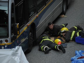 Firefighters work to remove the body of a cyclist from under a bus after the 61-year-old fell in front of the vehicle and was killed instantly on the Stanley Park Causeway on May 25. (Arlen Redekop/PNG FILES)