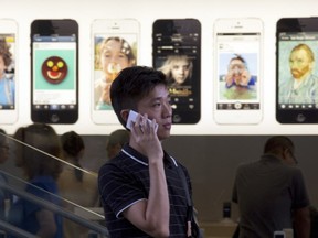 A Chinese man uses a non-Apple branded mobile phone outside a store with iPhone advertisements in Beijing.