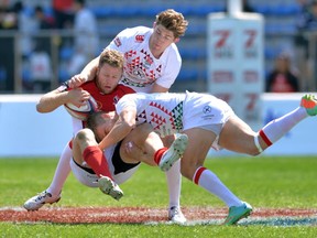 Canada's Conor Trainor (C) is tackled by England's players Tom Mitchell (R) and Phil Burgess (top) during their Tokyo Sevens 2014 Cup quarter-final match, part of the Rugby Sevens World Series, in Tokyo on March 23, 2014.   KAZUHIRO NOGI/AFP/Getty Images