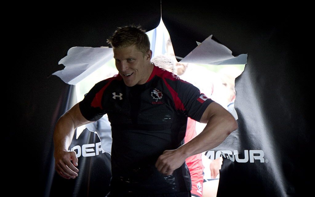 Rugby Canada men's team member John Moonlight bursts through a paper door as he shows off the team's new uniform at the team's practice facility in Burnaby, B.C. Tuesday, June, 3, 2014. THE CANADIAN PRESS/Jonathan Hayward ORG XMIT: JOHV109