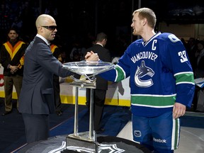 Injured Vancouver Canuck Manny Malhotra shakes hands with teammate Henrik Sedin beside the Presidents' trophy in 2011.