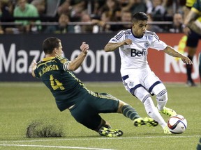 Portland Timbers midfielder Will Johnson, left, slides in on Vancouver Whitecaps midfielder Cristian Techera during the second half of an MLS soccer game in Portland.  (AP Photo/Don Ryan)