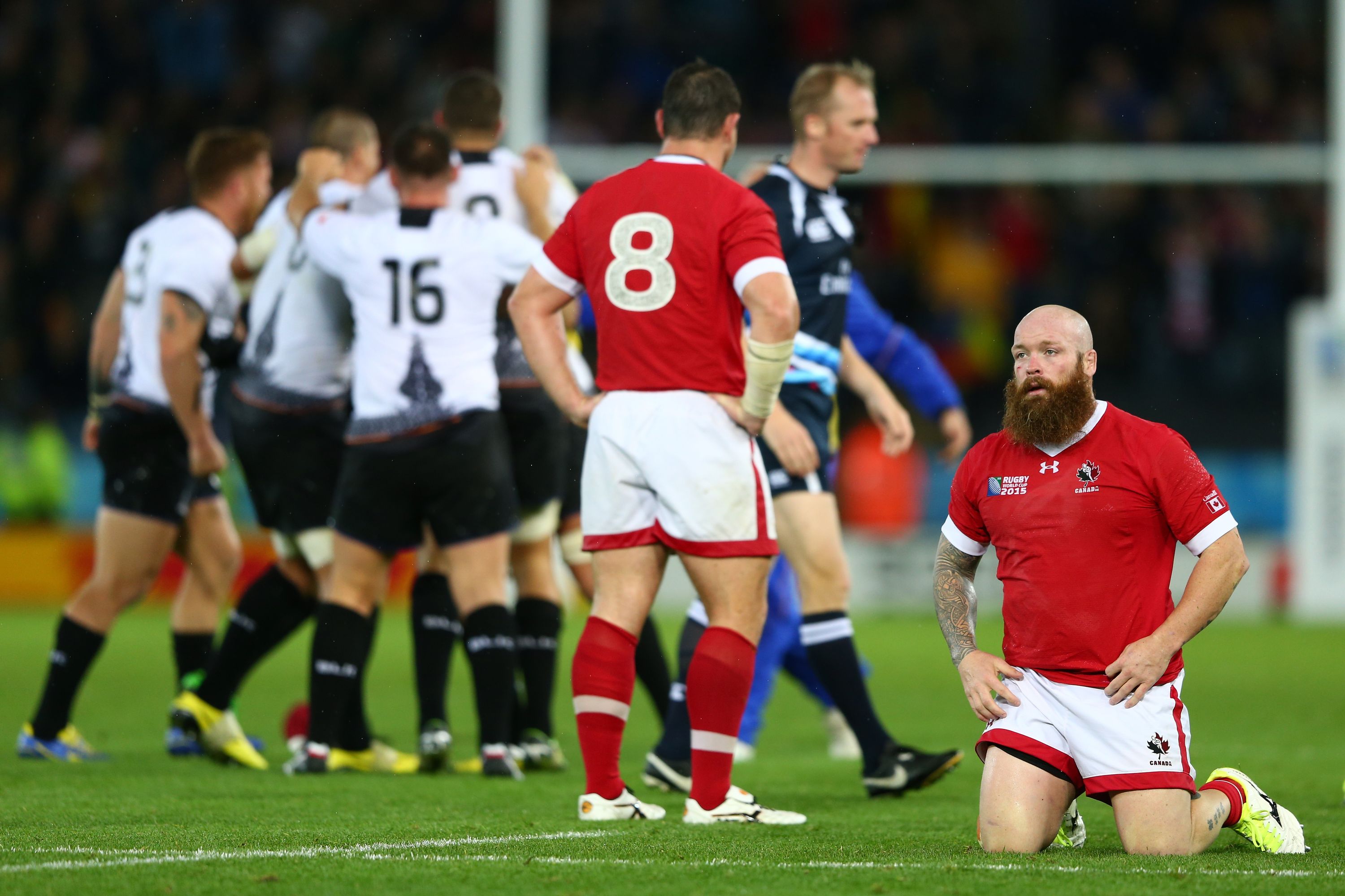 LEICESTER, ENGLAND - OCTOBER 06:  Ray Barkwill (R) and Aaron Carpenter (8) of Canada look dejected as Romania players celebrate after the 2015 Rugby World Cup Pool D match between Canada and Romania at Leicester City Stadium on October 6, 2015 in Leicester, United Kingdom.  (Photo by Michael Steele/Getty Images)