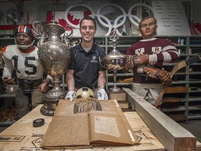 Curator Jason Beck with Lois Fisher's scrapbook from UBC women's 1930 basketball team, a 1970 Vancouver Canucks puck that was dropped for their first opening face-off, the Buchanan Cup trophy (for rowing) and Whitecaps’ 1979 NASL trophy, mannequins of B.C. Lions player Willie Fleming (far left) and Vancouver Millionaires’ Cyclone Taylor (far right).