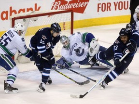 Winnipeg Jets' Dustin Byfuglien (33) tries to backhand the puck past Vancouver Canucks' goalie Jacob Markstrom (25) as Alex Biega (55) battles with Mark Scheifele (55) during third period NHL hockey action in Winnipeg, Tuesday, March 22, 2016. THE CANADIAN PRESS/Trevor Hagan
