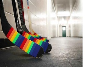 Hockey sticks adorned with Pride Tape line an arena corridor.