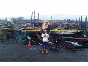 Micaela Robinson, owner of Loranda Stables & Kitty Kottage, stands with her daughter Lexy near their destroyed barn. The barn caught fire Thursday night and neighbours helped Robinson rescue all 16 horses and 10 cats that were inside.