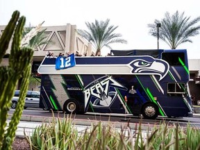 In this Saturday, Jan. 31, 2015 photo, cactuses frame rowdy fans hanging from the upper deck of "The Beast Bus" as the vehicle trundled through downtown Phoenix following the Seattle Seahawks Fan Fest at Chase Field in Arizona.