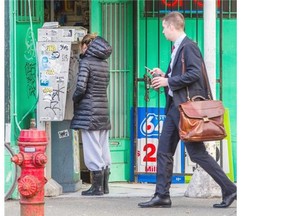 A woman uses a pay phone on the corner of Main and Cordova streets as a man walks by with a cellphone in his hand in Vancouver on Monday. Ric Ernst/ PNG