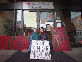 Two women sit outside the offices of the National Energy Board after locking themselves to the doors by placing bike locks around their necks, to protest the Kinder Morgan Trans Mountain Pipeline expansion, in Vancouver, B.C., on Monday January 18, 2016.