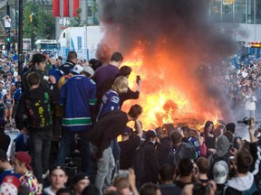 Vancouver Canucks fans watch a car burn during a riot following game 7 of the NHL Stanley Cup final in downtown Vancouver, B.C., on June 15, 2011.