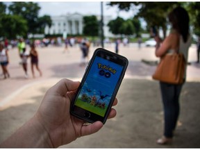 A man holds up his cellphone with the Pokemon Go game as a woman searches on her cellphone for a Pokemon in front of the White House in Washington.