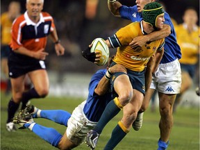 Wallaby inside centre Matt Giteau (C) passes the ball while being brought down by Italy's fullback Gert Peens (L) and Pablo Canavosio (R) during the rugby union Test between Australia and Italy at the Telstra Dome in Melbourne, 25 June 2005. The Australian Wallabies are currently leading Italy 69-21 in the second half.