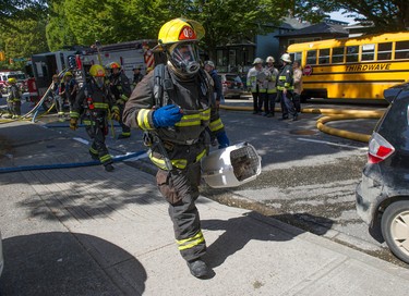 A firefighter carries a cat in its cage to safety down the sidewalk outside the house.