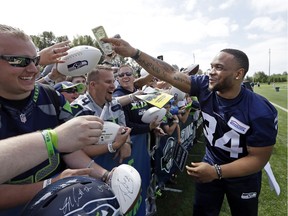 Seattle Seahawks' Thomas Rawls returns a dollar bill that he autographed after playfully threatening to keep it after the team's NFL football training camp Saturday, July 30, 2016, in Renton, Wash.