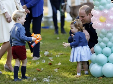 Britain's Prince William and Princess Charlotte look on as Prince George plays with a bubble gun at a children's party at Government House in Victoria, British Columbia, Thursday, Sept. 29, 2016.