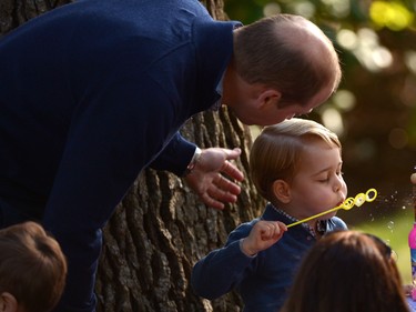 Prince George plays with bubbles as Prince William looks on during a children's tea party at Government House in Victoria, Thursday, Sept. 29, 2016.