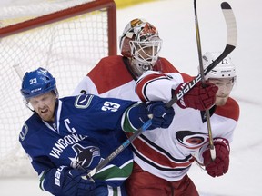 Carolina Hurricanes defenceman Brett Pesce (22) fights for control of the puck with Vancouver Canucks centre Henrik Sedin (33) as Carolina Hurricanes goalie Eddie Lack (31) looks on during third period NHL hockey action in Vancouver, B.C., on Sunday, Oct. 16, 2016.