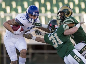 UBC's Will Watson, left,  tries to break away from University of Regina Rams Cord Delinte and Korey Greene during Canada West playoff football action at Mosaic Stadium on Saturday.