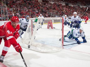 Luke Glendening of the Red Wings skates around the net for the puck as Ryan Miller and Troy Stecher defend the net.