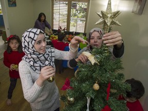 Mom Nisreen Aljabawi (right) and daughter place a star on the Christmas tree delivered to their family by MOSAIC settlement outreach worker Vian Saed (back).