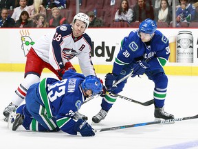 Boone Jenner #38 of the Columbus Blue Jackets and Jannik Hansen #36 of the Vancouver Canucks watch the puck slip past Henrik Sedin #33 of the Canucks during their NHL game at Rogers Arena December 18, 2016 in Vancouver, British Columbia, Canada.